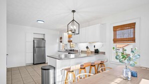 A modern kitchen with white cabinets, a stainless steel refrigerator, a central island with bar stools, and a hanging light fixture. - Lux 4br 3ba, hot tub, stargazing, HUGE gameroom, 10 min to Summersville Lake (Summersville)