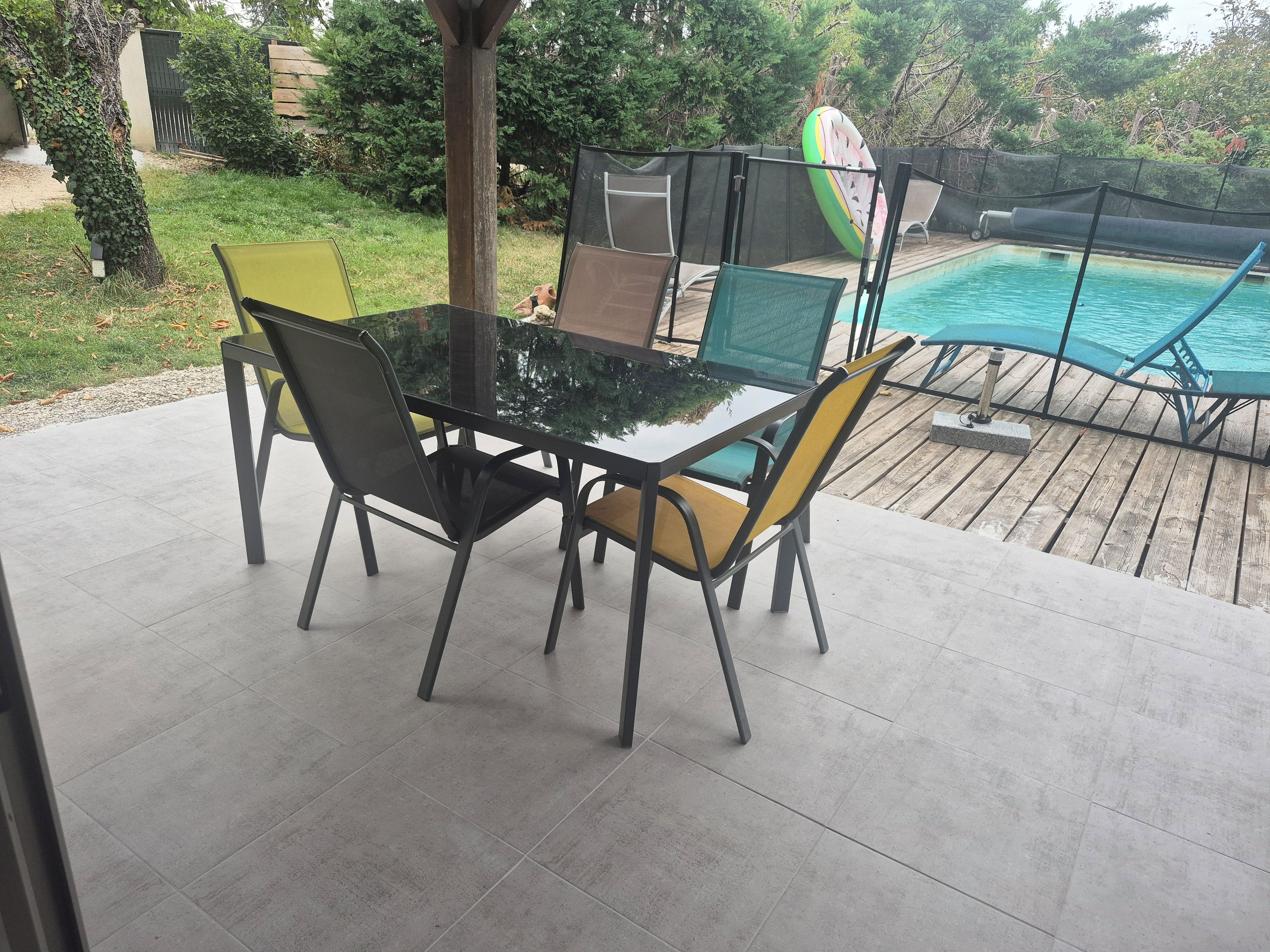 Un patio con mesa y sillas de vidrio, una piscina y una terraza de madera.