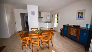 A dining area with a wooden table and chairs, a kitchen in the background, and a blue cabinet with glass doors. - Villa Pech DE Durand Villeneuve SUR LOT Acces PMR (Villeneuve-sur-Lot)