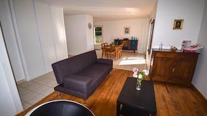 A living room with a sofa, a dining table with chairs, a wooden cabinet, and a small table with a vase of flowers. - Villa Pech DE Durand Villeneuve SUR LOT Acces PMR (Villeneuve-sur-Lot)