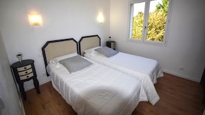 A bedroom with two beds, a nightstand, a wall-mounted light, and a window with a view of trees. - Villa Pech DE Durand Villeneuve SUR LOT Acces PMR (Villeneuve-sur-Lot)