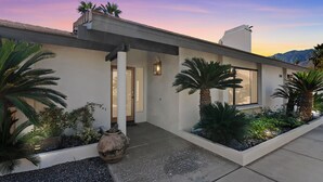 Una casa moderna con techo plano, ventanas amplias y un jardín cuidado con palmeras y una maceta grande.
