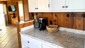 A kitchen with white cabinets, a coffee maker, and a basket on the counter. - Sea Captain's Cottage 2; Oceanfront Cottage Court (Kill Devil Hills)
