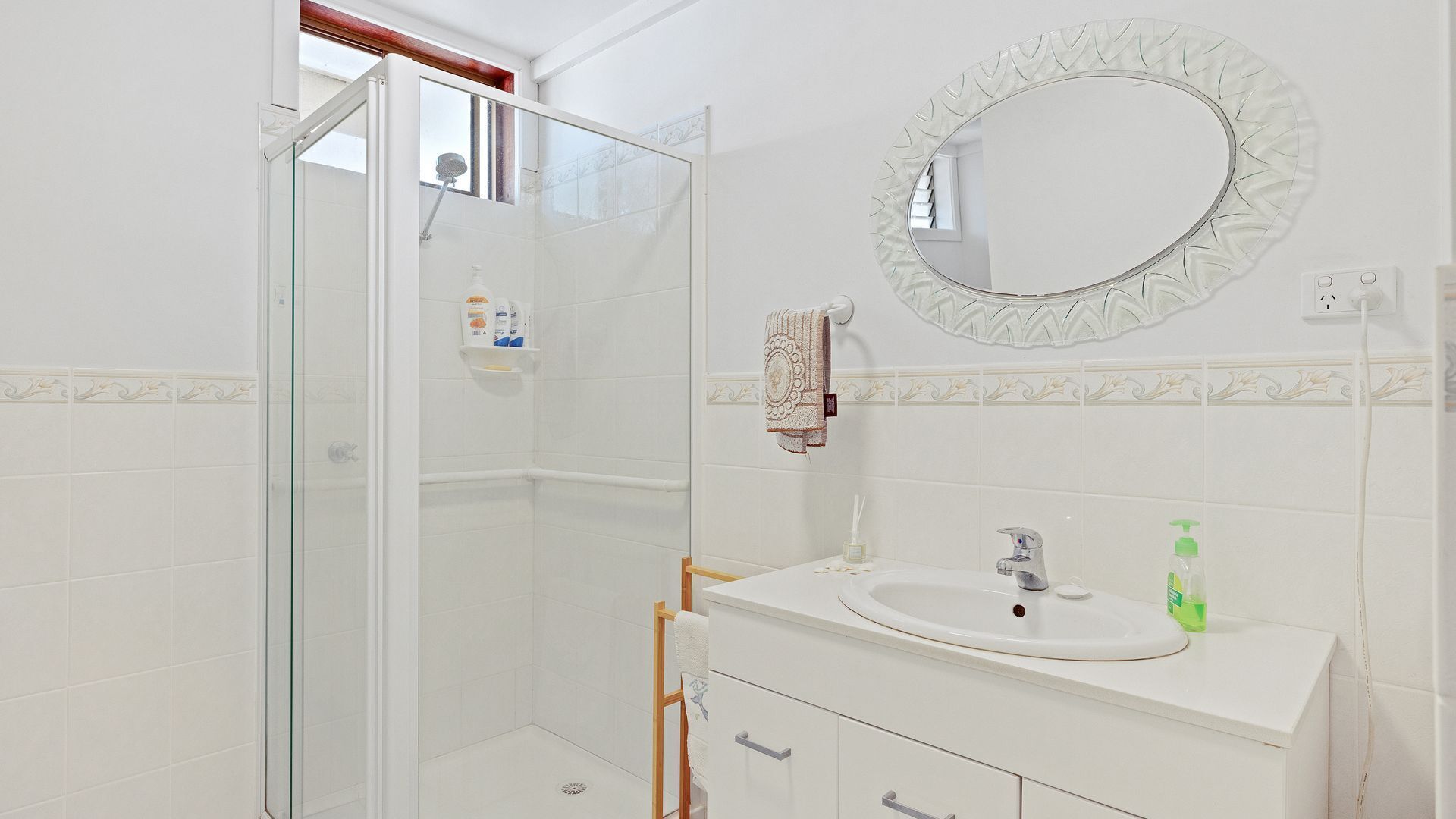 A bathroom with a glass shower enclosure, a white sink with a mirror above it, and a towel hanging on a rack.