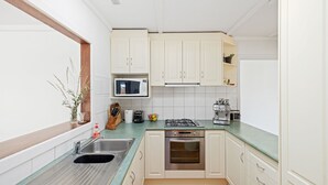 Une cuisine de taille réduite, dotée de meubles blancs, d’une cuisinière à gaz, d’un four, d’un four à micro-ondes et d’un évier.