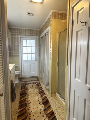 Un pasillo con alfombra estampada, una puerta y un inodoro blancos, y una zona de ducha.