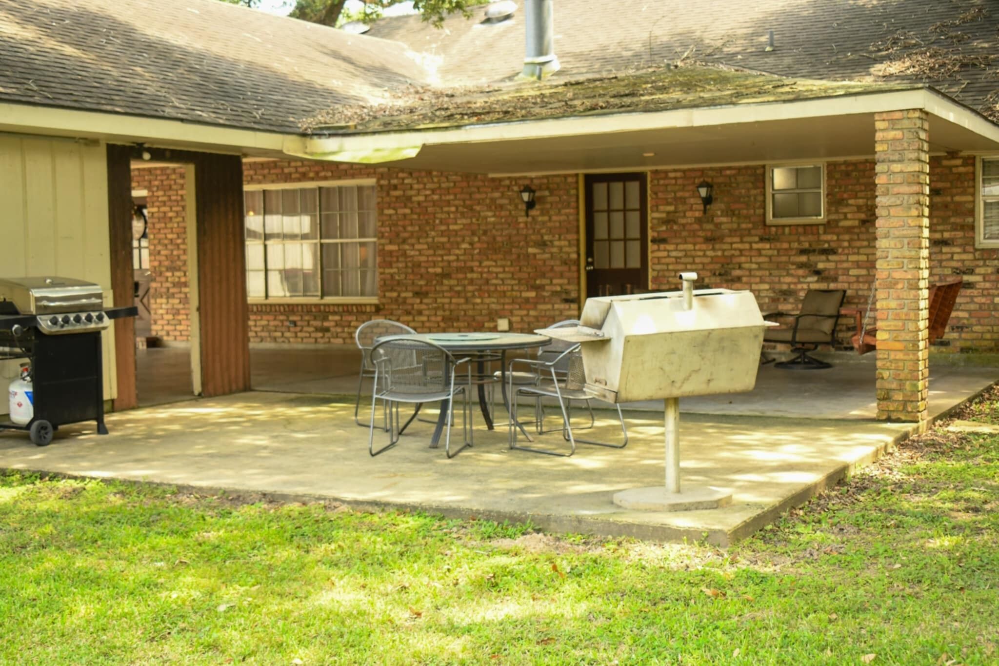 A backyard with a barbecue grill, a table with chairs, and a covered patio area.