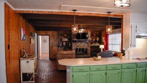 Une cuisine dotée d’une cheminée en pierre, de meubles de couleur verte et de luminaires suspendus.