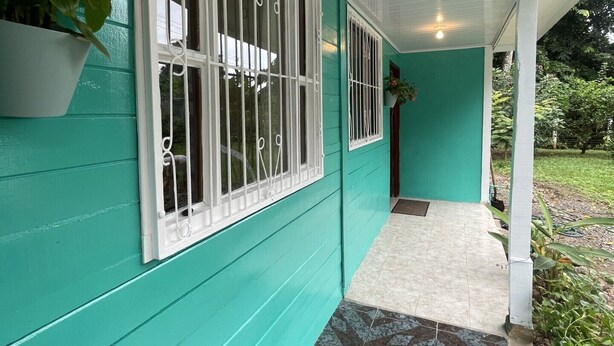 A covered porch with a tiled floor and a window with white bars. - Casa Rio Verde, a great place for family and friends , surrounded by nature! (Cahuita)