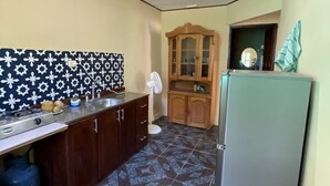 A compact kitchen with a patterned backsplash, a built-in stove, a refrigerator, and a wooden cabinet. - Casa Rio Verde, a great place for family and friends , surrounded by nature! (Cahuita)