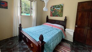 A bedroom with a bed, a window with curtains, a painting on the wall, and a door. - Casa Rio Verde, a great place for family and friends , surrounded by nature! (Cahuita)