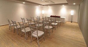 Een vergaderzaal met rijen stoelen, een tafel met een witte tafelkleed en een rode bloemstelling.