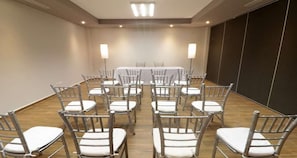 Een congreszaal met een lange tafel, stoelen en staande lampen.