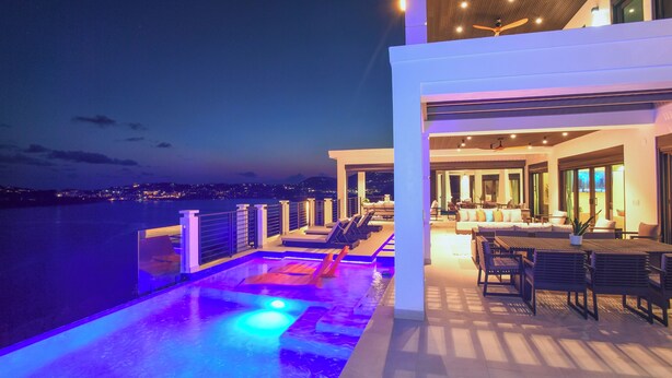 A modern hotel with a rooftop pool, outdoor seating, and a view of the city at night. - Luxury Villa in Cabrita Point- Sky View Villa with Pickleball & Basketball Court (ST THOMAS)