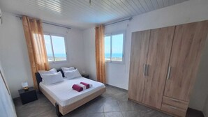 Ein Schlafzimmer mit einem Bett, Nachttischen, einem Kleiderschrank und großen Fenstern.