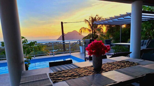 Ein Poolbereich mit Blick auf das Meer und ein Berg bei Sonnenuntergang.