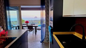 Eine moderne Küche mit Meerblick, ein Essbereich mit Tisch und Stühlen sowie ein großes Fenster mit Vorhängen.