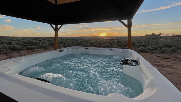 Un jacuzzi bajo una pérgola de madera con un paisaje desértico y la puesta de sol al fondo.