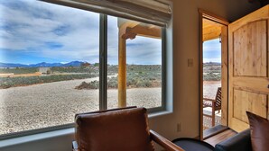 Una habitación con un amplio ventanal que ofrece vistas a un paisaje desértico, una puerta de madera y un sillón de cuero.