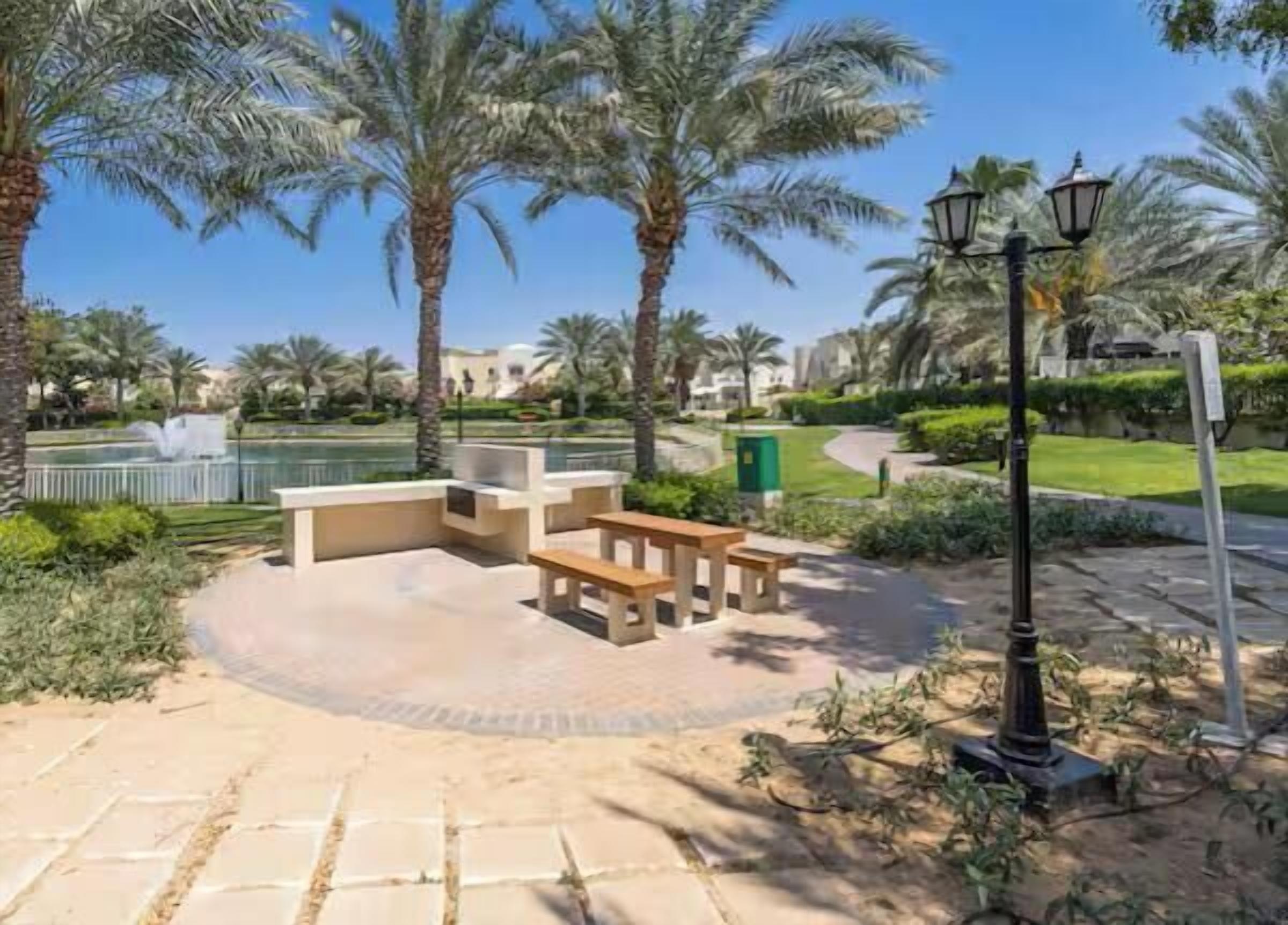 A circular outdoor seating area with benches, surrounded by palm trees and a fountain.