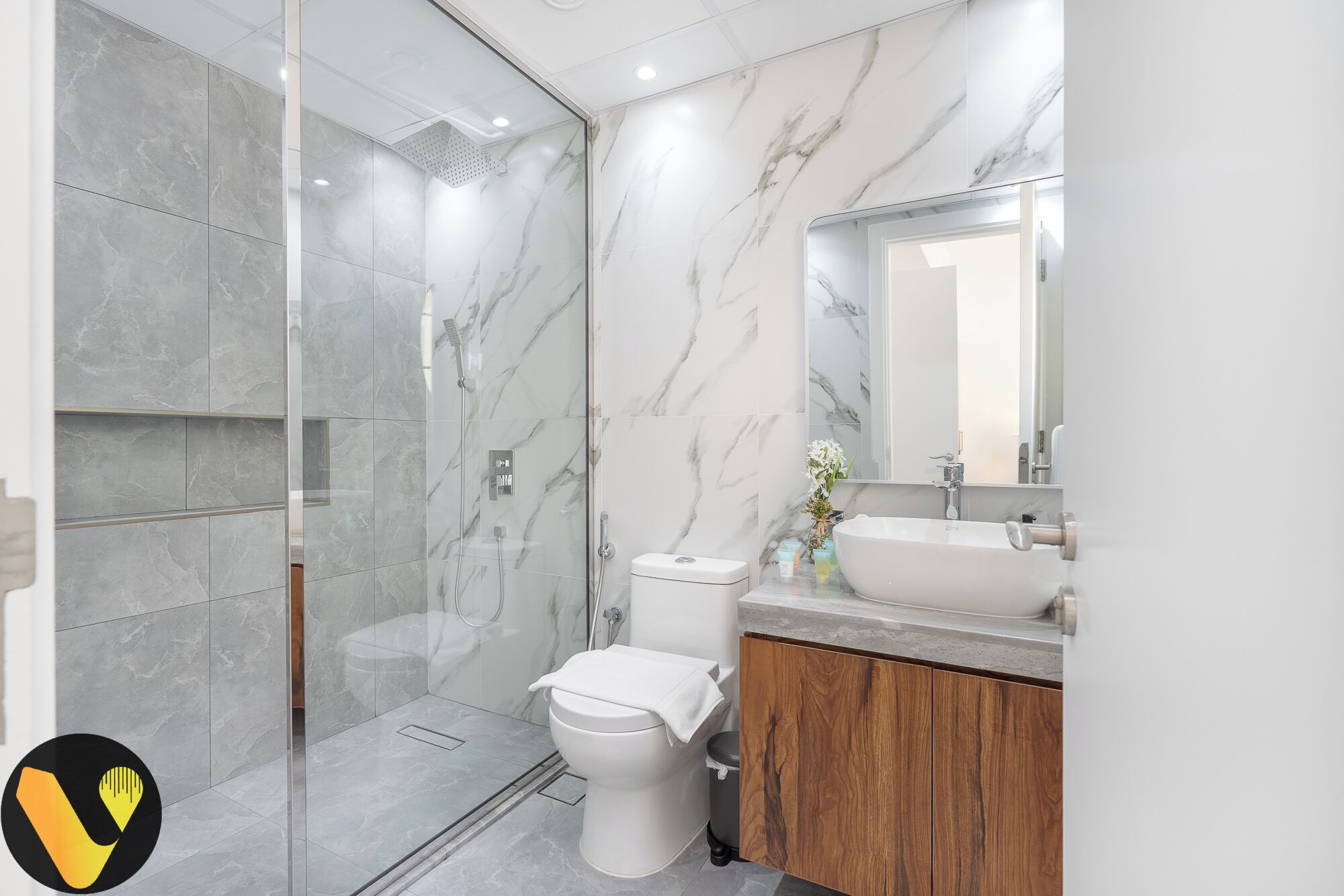 A modern bathroom with a glass-enclosed shower, a toilet, and a vanity with a sink and mirror.