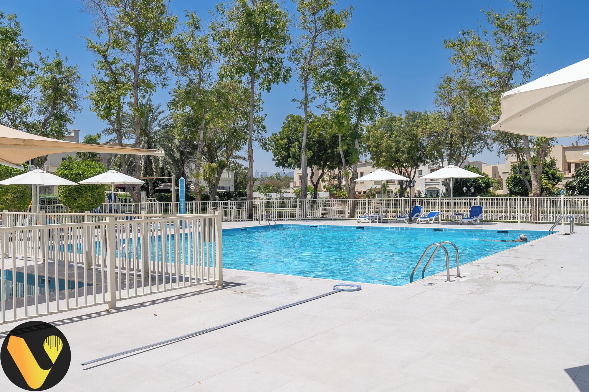 A swimming pool with a white fence, lounge chairs, and umbrellas.