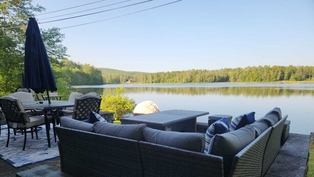 Une terrasse dotée de meubles en osier, d’une table et d’un parasol, offrant une vue sur un lac.