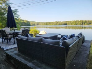 Un patio con mobiliario de mimbre, una mesa y una sombrilla con vistas a un lago.