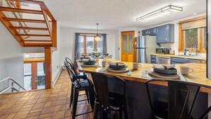 Une cuisine moderne avec un îlot central en bois, des tabourets de bar et une vue sur l’extérieur.