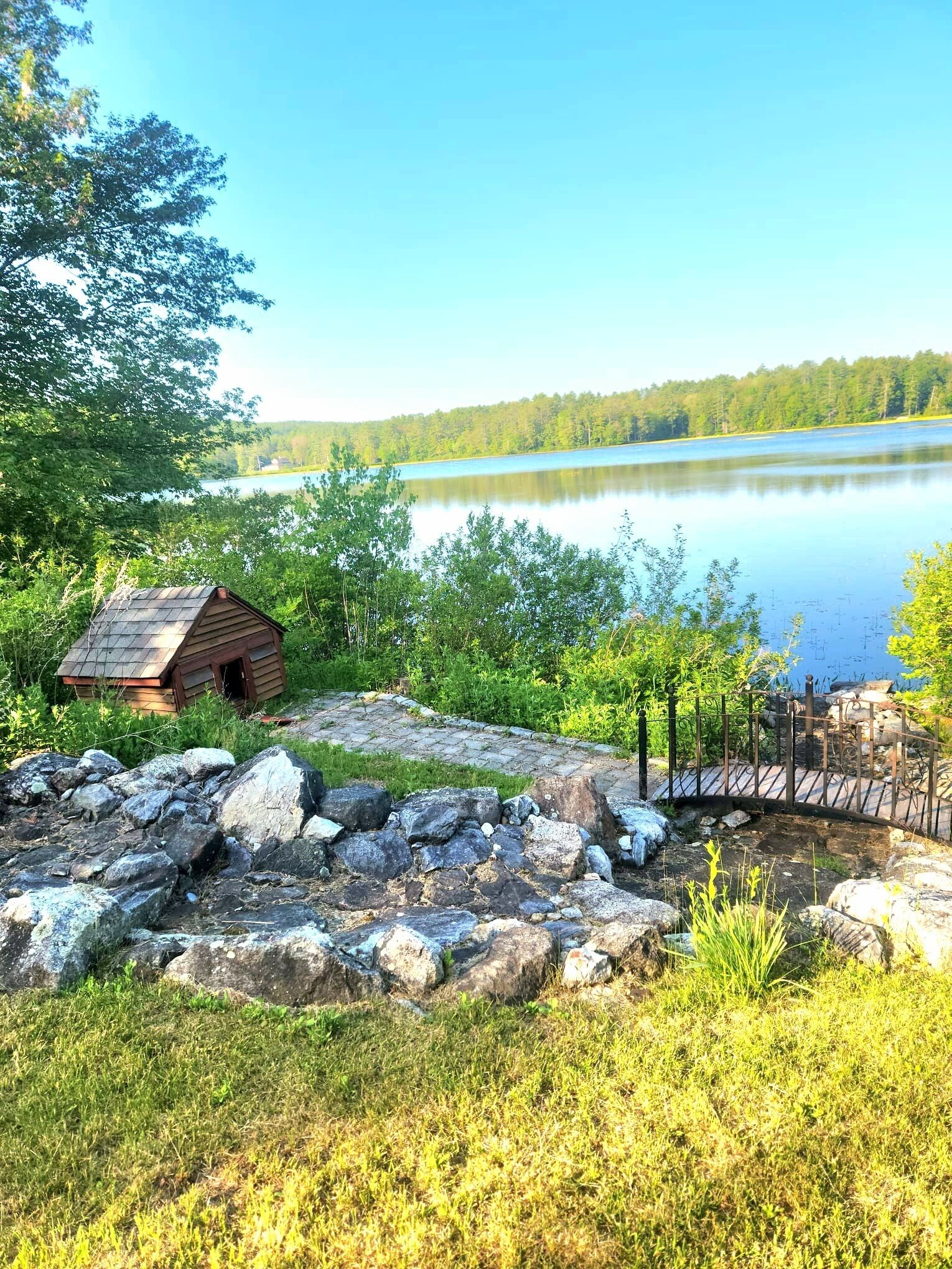 A rustic cabin by a lake with a wooden deck and a metal fence.