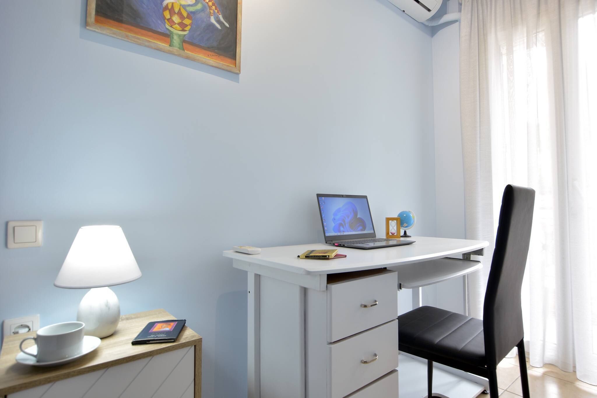 A room with a desk, a laptop, a globe, a lamp, a cup, and a book.