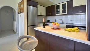 A modern kitchen with dark cabinets, a stainless steel refrigerator, a bowl of fruit, and a bottle of wine on the counter. - Corfu SeaTy Apartment (Corfu)
