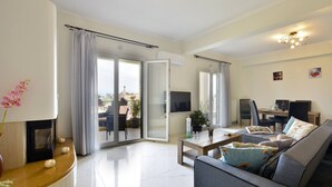 A modern living room with a sofa, a coffee table, and a fireplace. There is a sliding glass door leading to an outdoor area. - Corfu SeaTy Apartment (Corfu)