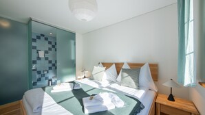 Et moderne hotelværelse med en stor seng, en glasbrusekabine, et trænatbord og udsigt over byen.