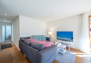 Uma sala de estar moderna com um sofá cinzento, uma televisão de tela plana e uma mesa de centro branca.