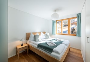 Uma cama bem arrumada com cabeceira de madeira, mesa de cabeceira com abajur e janela com cortinas.