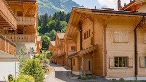 En række traditionelle træhuse med balkoner, foran et bjerglandskab og en klar himmel.