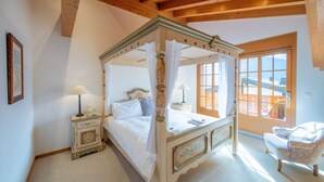 Una cama con dosel y cuatro columnas, con una mesita de noche, una silla y un ventanal con vistas al exterior.