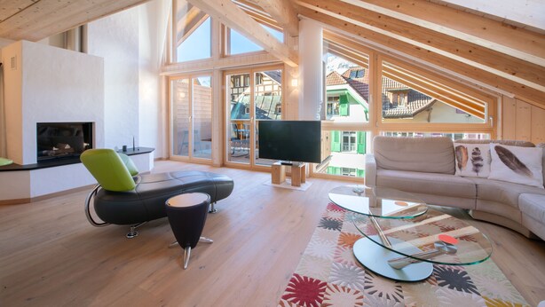 A spacious living room with a high ceiling, wooden beams, a large TV, a sofa, a coffee table, and a fireplace.