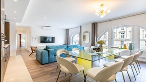 Un salon moderne avec une table à manger en verre, un canapé bleu et un téléviseur fixé au mur.