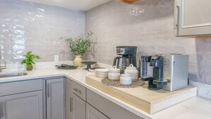 Moderni keittiö, jossa on harmaat kaapit, valkoinen työtaso, kahvinkeitin, leivänpaahdin ja ruukkukasvi.
