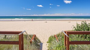 Ein Strand mit einer Holzpromenade, die zum Ufer führt, umgeben von Gras und Pflanzen.