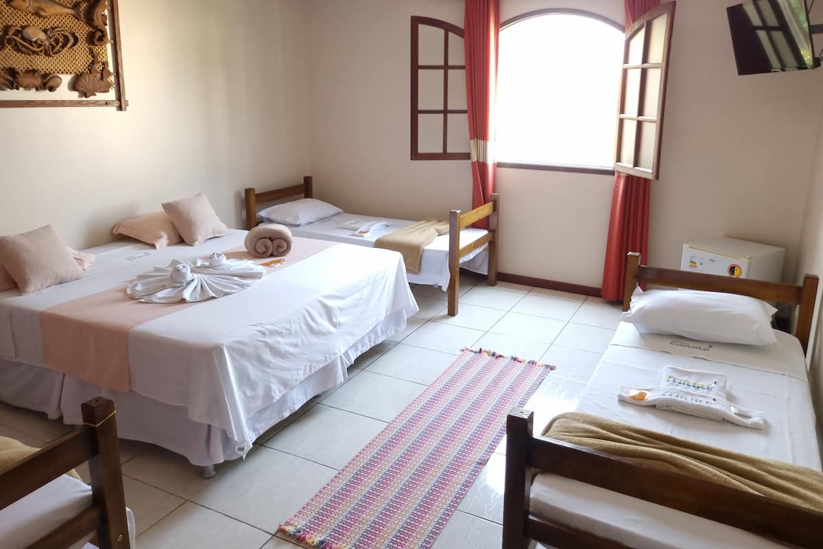 A hotel room with two single beds, a wooden headboard, a window with red curtains, a small table with a towel, and a wall-mounted artwork.