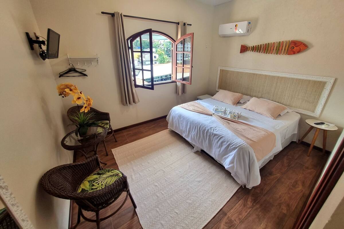 A bedroom with a bed, a desk, a chair, a window with curtains, and a wall-mounted air conditioner.