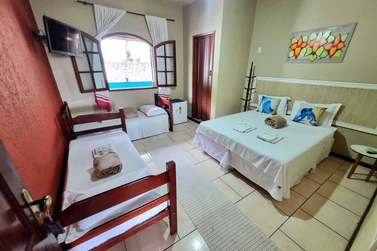 A hotel room with two beds, a TV, a window with curtains, a painting on the wall, and a small table.