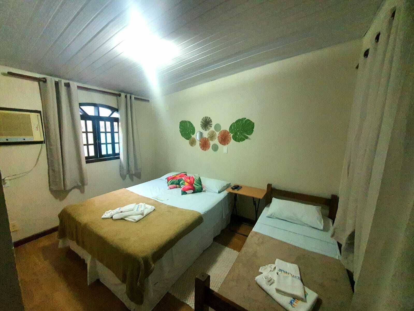 Habitación de hotel con dos camas, una ventana con cortinas, un adorno de hojas tropicales en la pared y una pequeña mesa con una silla.