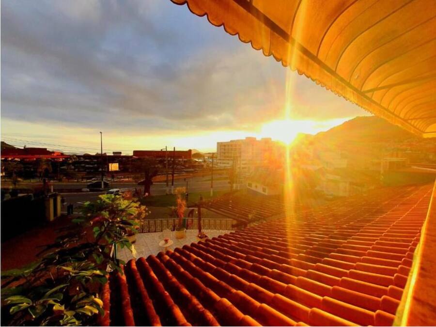 Vista do pôr do sol a partir de um terraço coberto, com piso de azulejos e plantas em vasos.
