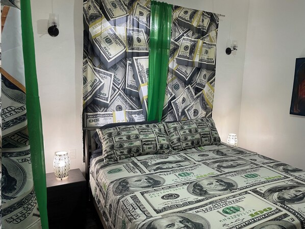 A bed with a $100 bill pattern, a green curtain, and a wall-mounted light fixture.