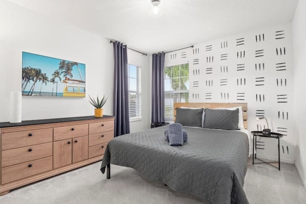 A modern bedroom with a bed, a dresser, a painting, and a window with curtains.