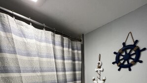 Un baño con cortina de ducha a rayas, un inodoro blanco y una decoración con timón de barco en la pared.
